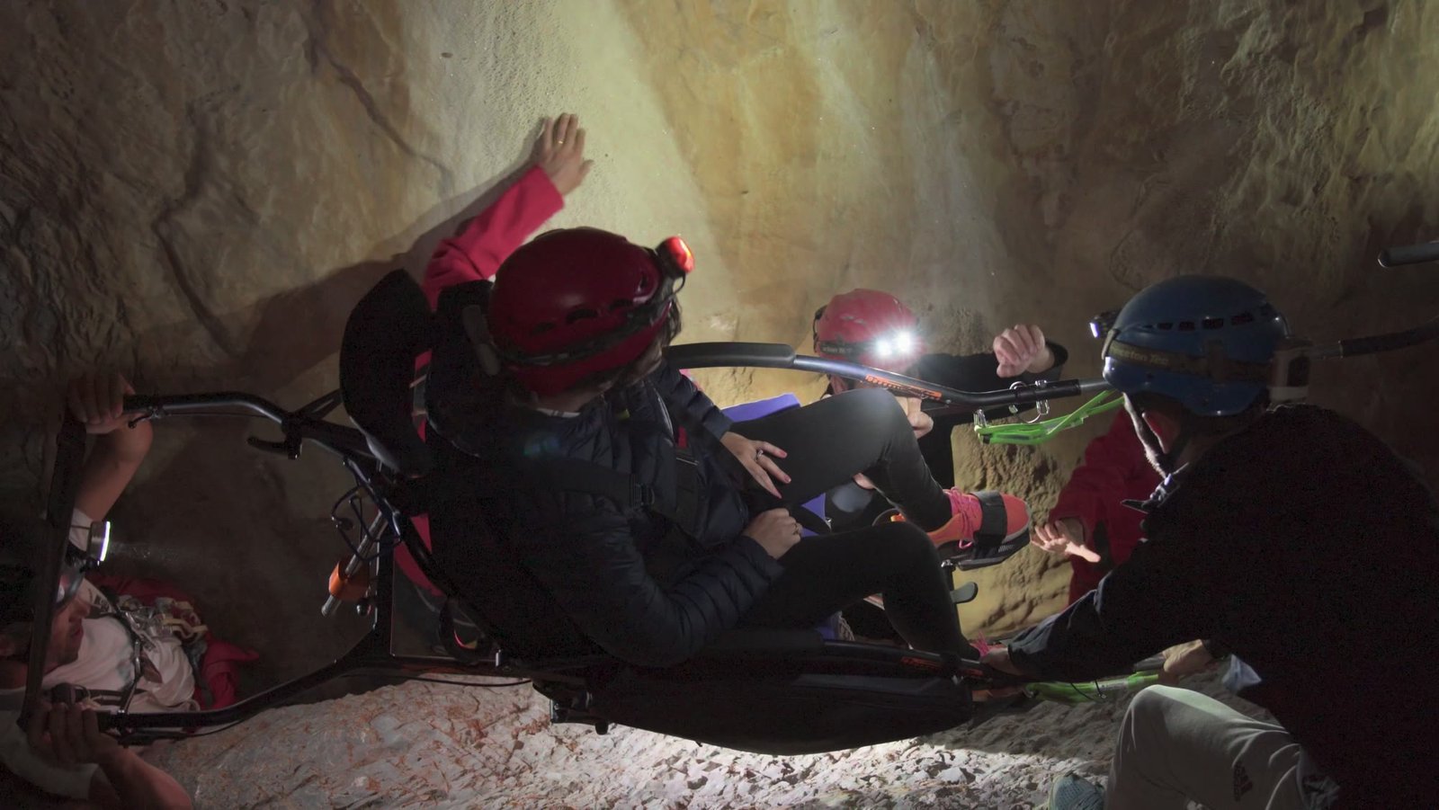 Marianne dans son fauteuil, sous terre, entourée de spéléologues